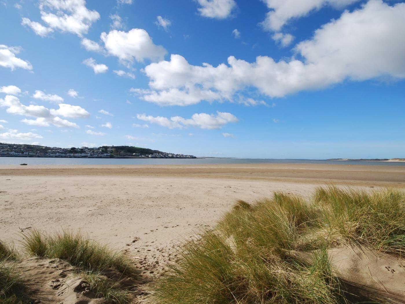 Ein Strand mit Dünen, einem klaren Himmel und einer entfernten Küstenlinie mit Gebäuden.