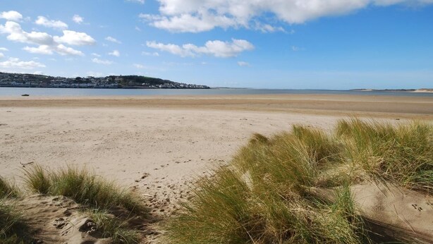 A beach with sand dunes, a clear sky, and a distant shoreline with buildings. - 2 Bed in Bideford (oc-infpb) (Westleigh)