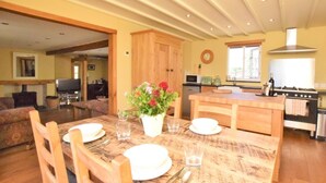 A dining area with a wooden table set for four, a kitchen in the background, and a living room with a sofa. - 2 Bed in Barnstaple (oc-gcows) (Marwood)
