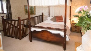 Ein Bett mit Himmelbett, ein Nachttisch aus Holz mit einer Lampe und ein gerahmtes Bild an der Wand.
