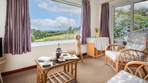 A room with a large window, wicker furniture, a small table with a coffee pot, and a dog. - 2 Bed in Falmouth (oc-tvean) (Constantine)