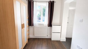 Quarto com radiador, guarda-roupa de madeira e janela com cortinas.