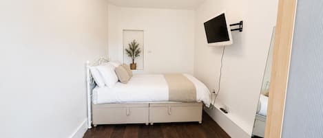 A bedroom with a bed, a mounted TV, a door, and a plant.