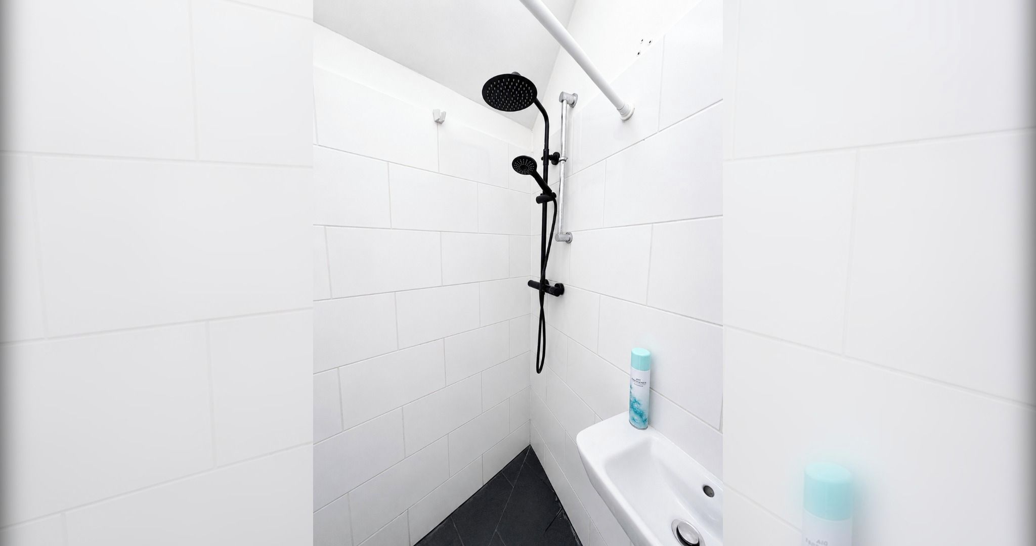 Ein Badezimmer mit weißen Fliesen, einem schwarzen Duschkopf und einer weißen Badewanne.