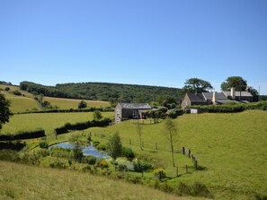A rural landscape with a small house, a pond, and rolling hills in the background. - 2 Bed in Dulverton (oc-threb) (East Anstey)