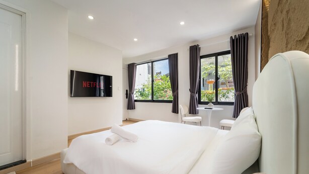 Una camera d'albergo moderna con un letto, una televisione, una finestra con tende e un piccolo tavolo.