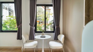 Una stanza con un tavolo bianco rotondo, due sedie bianche, una finestra con tende e vista su del verde all'esterno.
