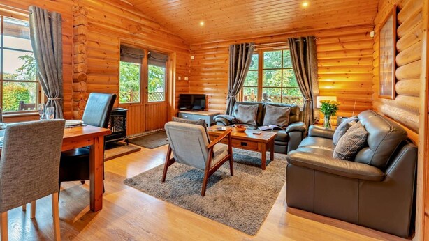 A log cabin interior with a dining area, a sofa, a TV, and a fireplace. - 3 Bed in Dunsyre (oc-lk15m) (Walston)