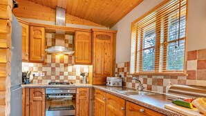 A kitchen with wooden cabinets, a stove, a sink, and a window with blinds. - 3 Bed in Dunsyre (oc-lk15m) (Walston)