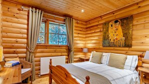 A log cabin bedroom with a wooden bed, a radiator, a window with curtains, a lamp, and a painting on the wall. - 3 Bed in Dunsyre (oc-lk15m) (Walston)