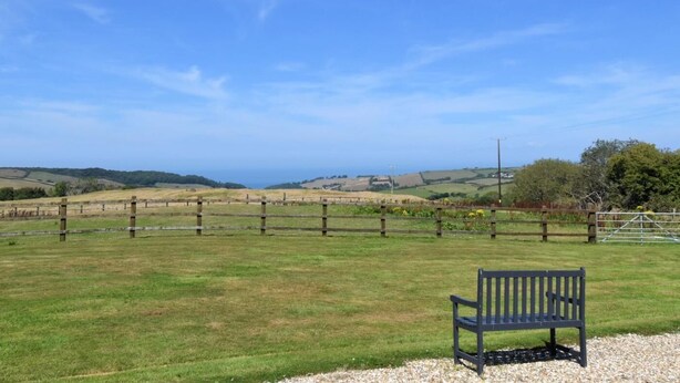 A bench in a grassy field with a wooden fence and distant hills. - 1 Bed in Ilfracombe (oc-parsc) (Berrynarbor)