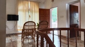 A room with a ceiling fan, a television mounted on the wall, a wooden chair, a wooden table, and a staircase. - Green Nestle Farmhouse  (Vaikom)
