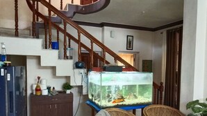 A living room with a fish tank, wooden staircase, and wicker chairs. - Green Nestle Farmhouse  (Vaikom)