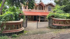 A two-story house with a red roof, surrounded by lush greenery and a gated entrance. - Green Nestle Farmhouse  (Vaikom)