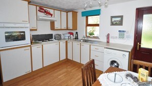 A compact kitchen with a stove, oven, sink, and a window with a view. - 1 Bed in Lairg (oc-su304) (Lochinver)