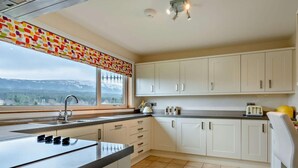 Una cocina con una isla grande, armarios blancos, un ventanal con vistas y piso de baldosas.