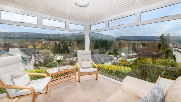 Un invernadero con vistas panorámicas a un valle, amoblado con un sofá, dos sillones y una mesita.