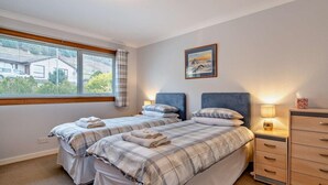 Un dormitorio con dos camas, una ventana con persianas, un cuadro en la pared y una mesita de noche con lámpara.
