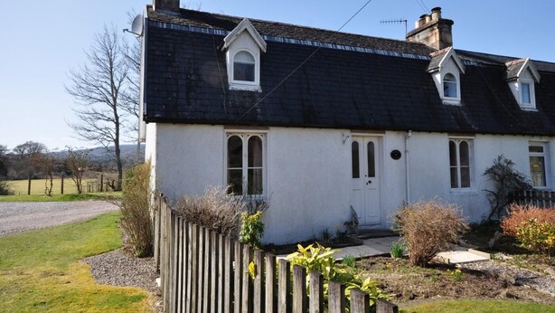 Ein zweistöckiges Haus mit dunklem Dach, weißen Wänden und einem Holzzaun davor.