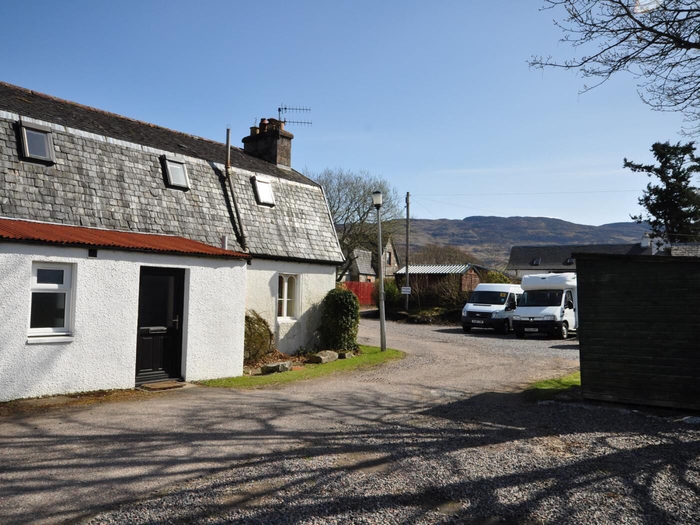 A rural road with a white house, a gravel driveway, and a parked white van.