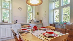 Una cucina con un tavolo da pranzo per quattro persone, un lampadario e vista su del verde all'esterno.