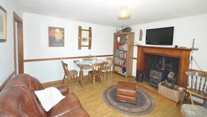 Ein Wohnzimmer mit Kamin, Fernseher, Esstisch mit Stühlen und einer Couch.