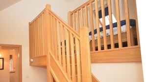 Uma escada de madeira com corrimão, que leva a um quarto com cama.