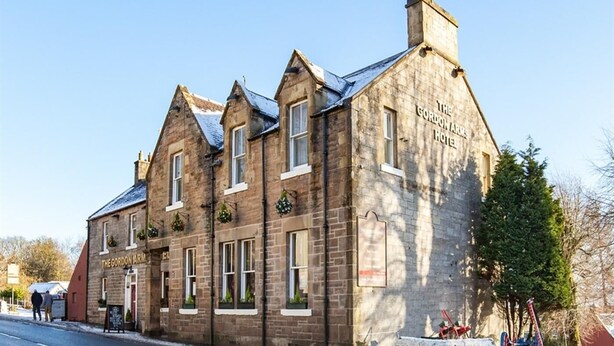 Um edifício histórico de pedra com várias janelas e uma placa com o nome 'The Gordon Arms Hotel'.