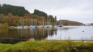 Un lago tranquillo con barche, circondato da alberi e colline.