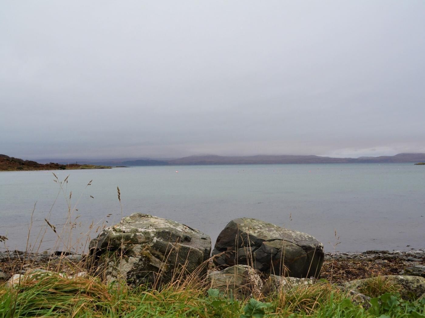 A calm lake with large rocks in the foreground and a distant shoreline.