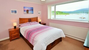 Una camera da letto con un letto, comodini, una finestra che offre vista su un lago e barche, e due quadri appesi al muro.