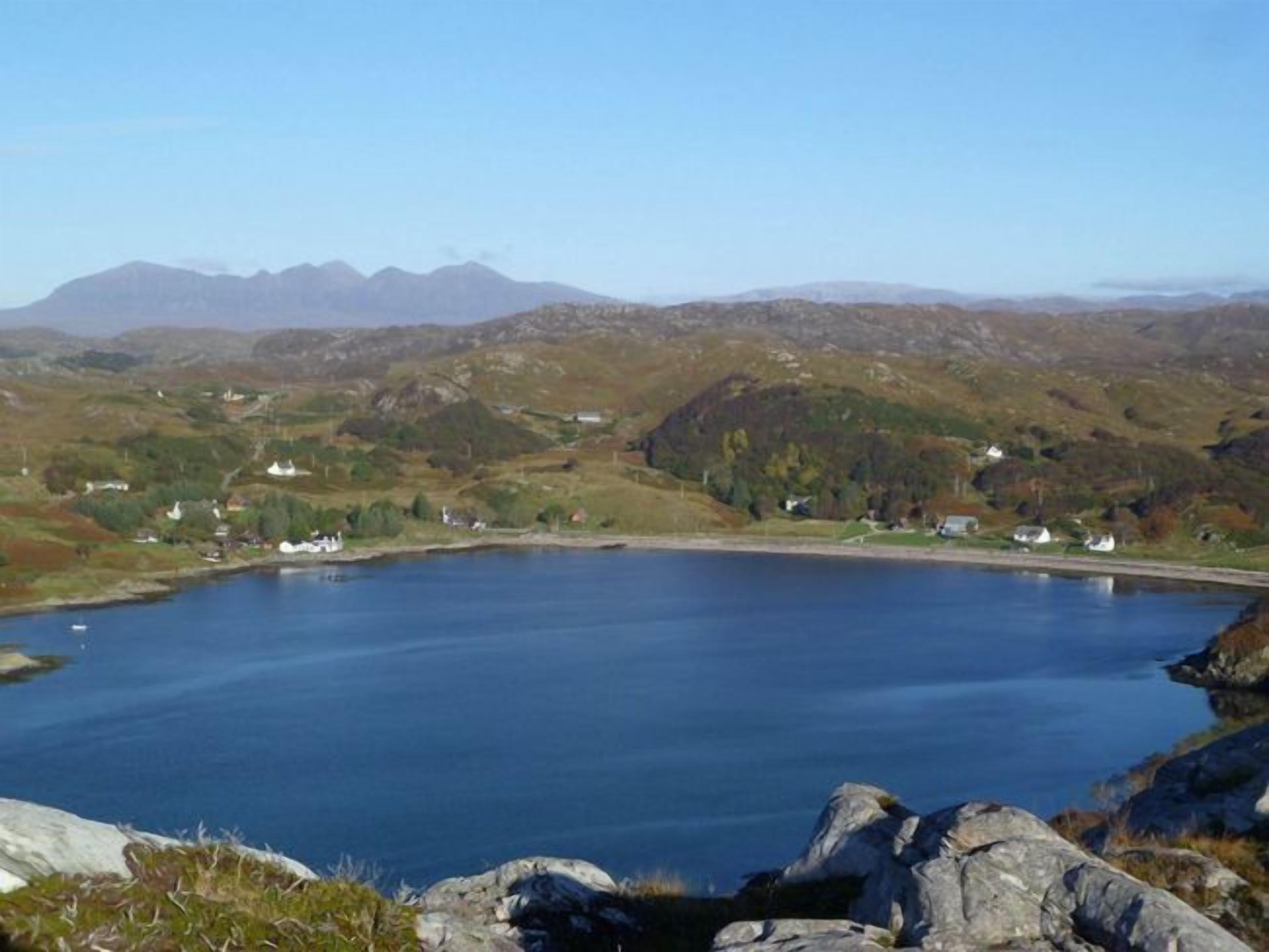 Un lac entouré de collines, avec quelques bâtiments visibles au loin.