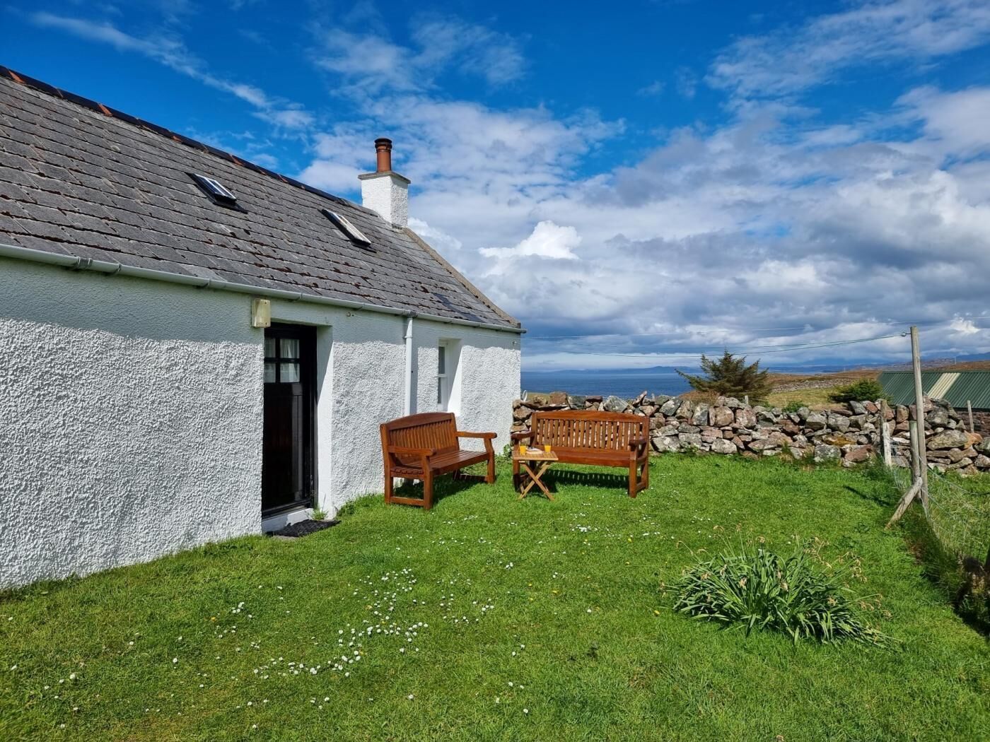 A white house with a grey roof, a stone wall, and a grassy yard.