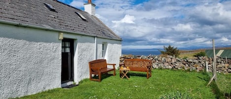 A white house with a grey roof, a stone wall, and a grassy yard.