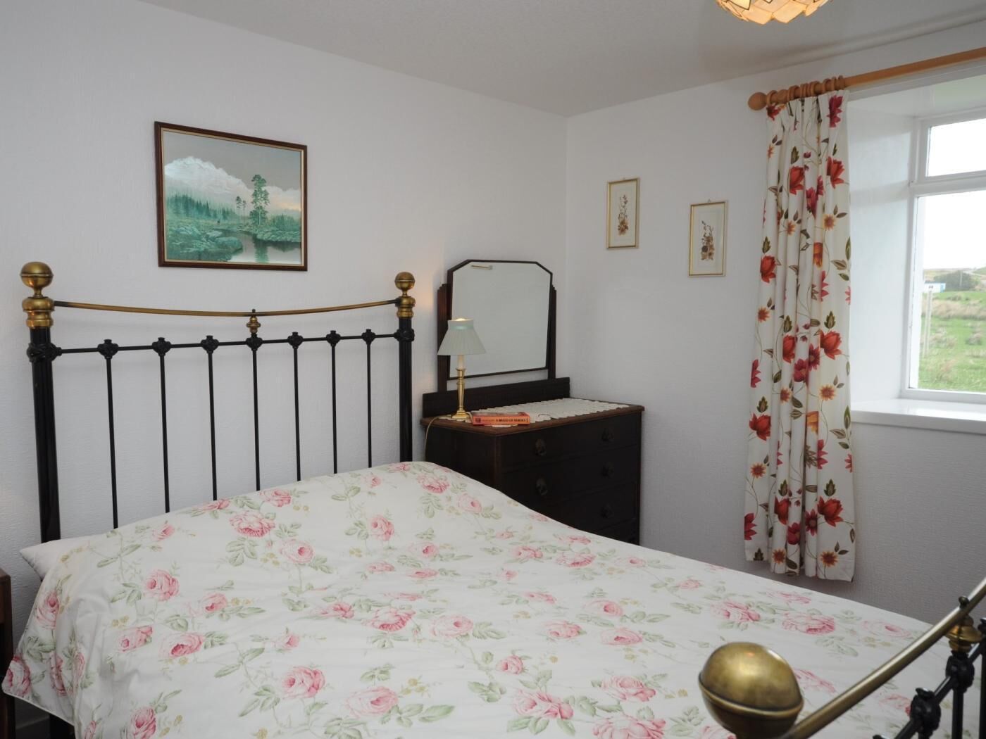A bedroom with a bed, a dresser, a mirror, and a window with floral curtains.