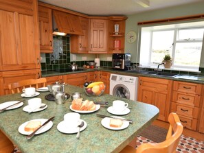 A kitchen with wooden cabinets, a washing machine, a coffee maker, and a dining table set with plates, cups, and utensils. - 2 Bed in Lairg (oc-su187) (Lochinver)