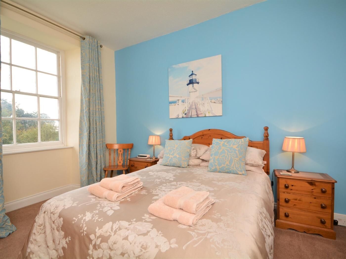 A bedroom with a bed, two bedside tables, a nightstand, a window with curtains, and a painting on the wall.