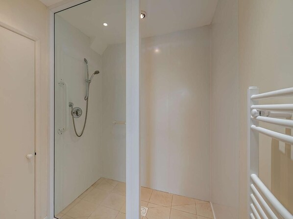 Un baño con cabina de ducha de vidrio, radiador blanco y suelo de baldosas.