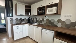 Une cuisine compacte avec des meubles blancs, un four à micro-ondes, un lave-vaisselle et un dosseret de carrelage hexagonal.