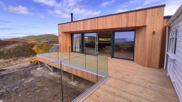 A modern house with a wooden exterior, large glass windows, and a deck. - 3 Bed in Lairg (oc-su164) (Scourie More)