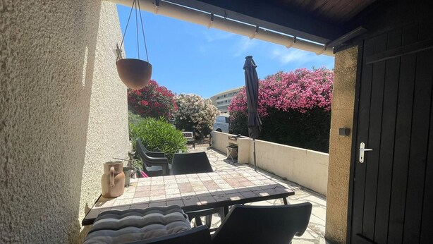 En uteplats med ett bord och stolar, en hängande blomkruka och en dörr.