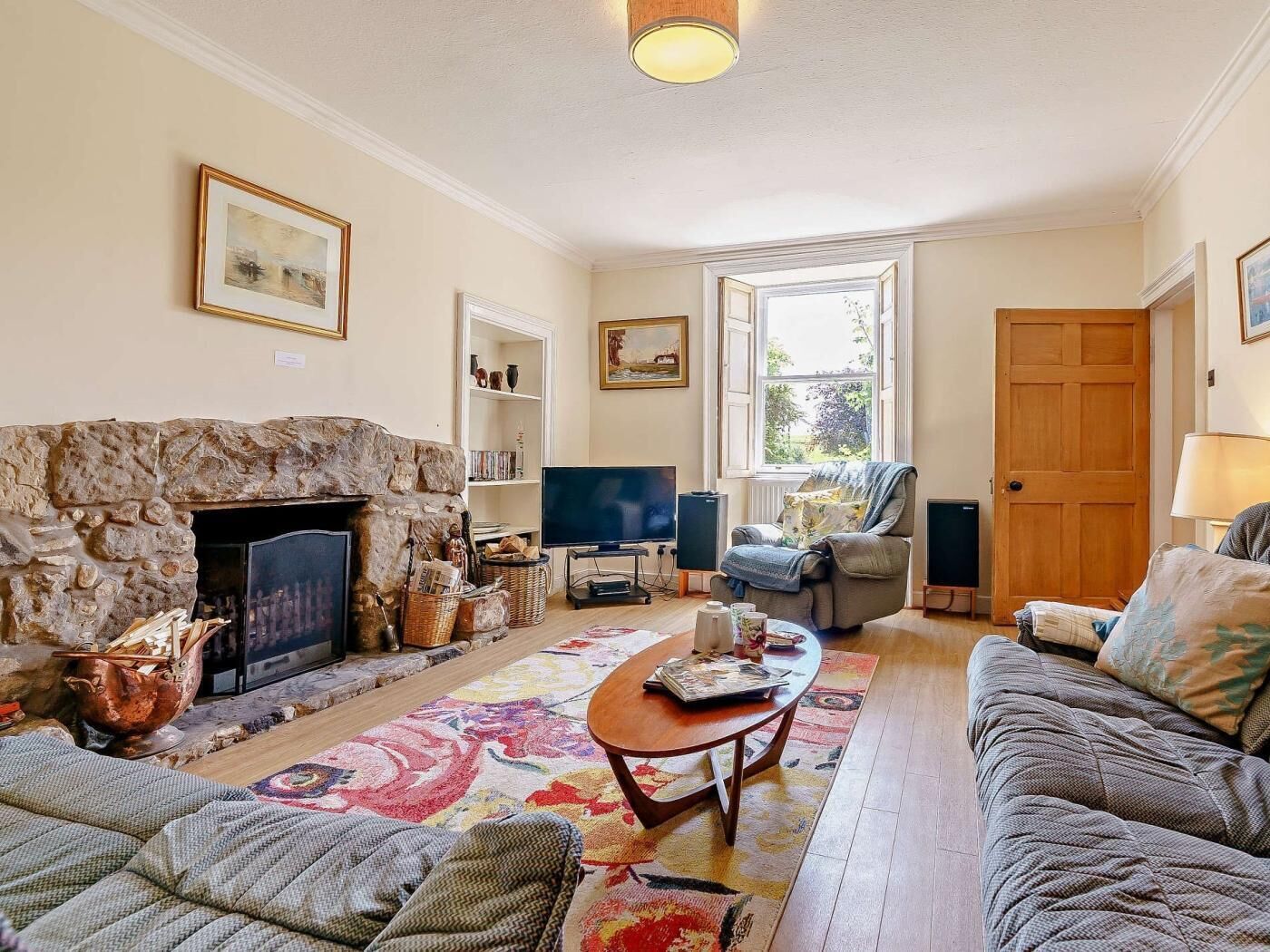 A living room with a stone fireplace, a television, a sofa, a chair, and a door.