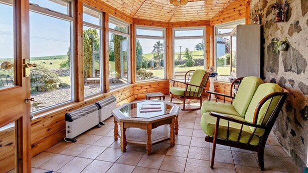 Ein Zimmer mit Holzwänden, großen Fenstern, einem Tisch, Stühlen und einer Heizung.