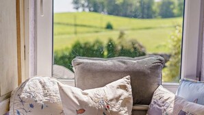 Ein Fensterplatz mit mehreren Kissen und Blick auf eine grüne Landschaft.