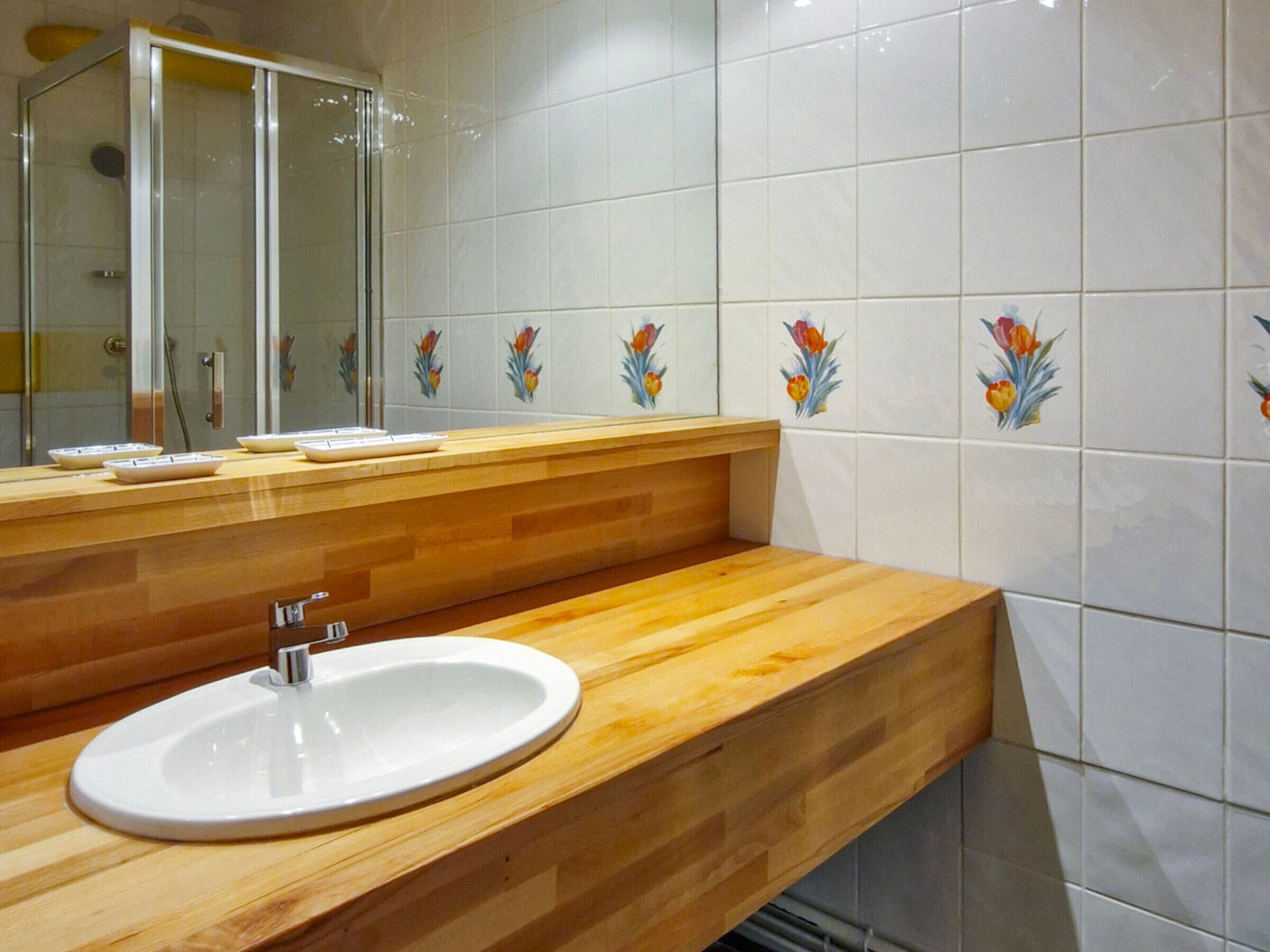 Ein Badezimmer mit Holzwaschtisch, weißem Waschbecken, einer Duschkabine aus Glas und Fliesenwänden mit floralem Muster.