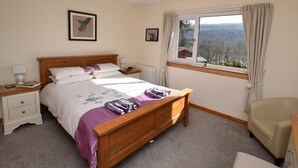 A bedroom with a wooden bed, a nightstand, a chair, a window with a view, and a hanging light fixture. - 3 Bed in Inverness (oc-in633) (Balnain)