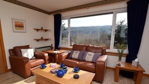 A living room with a sofa, armchair, coffee table, and a view of the outdoors. - 3 Bed in Inverness (oc-in633) (Balnain)