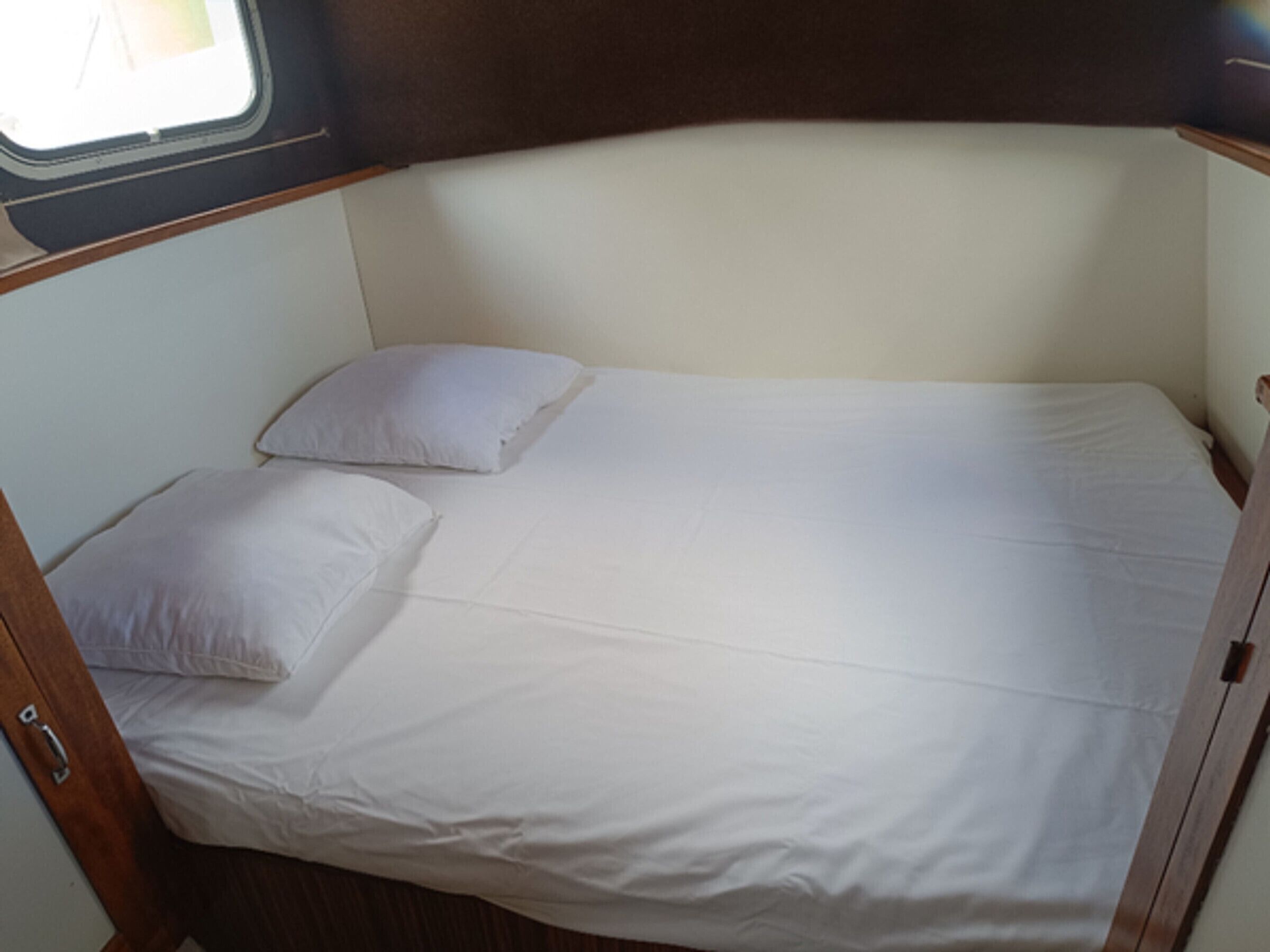 Un lit simple avec une literie blanche, dans une chambre aménagée dans un style rustique et dotée d’une fenêtre.