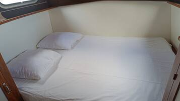Un lit simple avec une literie blanche, dans une chambre aménagée dans un style rustique et dotée d’une fenêtre.