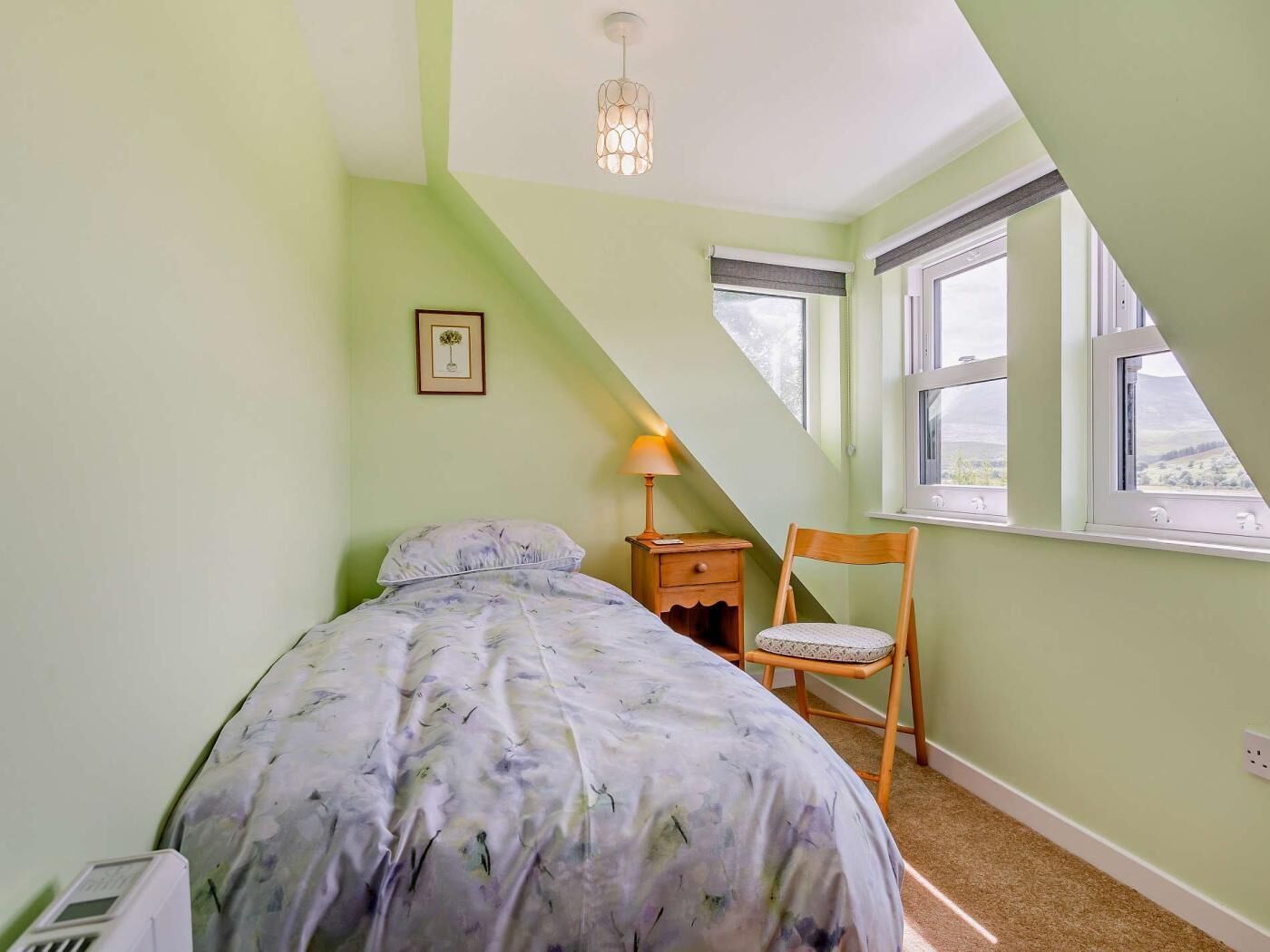 A bedroom with a bed, a nightstand, a chair, a lamp, and a window with a view.